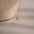 The Moonstone Charm Necklace features a gold chain with a small circular pendant, beautifully displayed on a neutral textured background—an elegant piece ideal for moonstone jewelry lovers.
