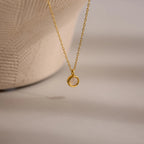 The Moonstone Charm Necklace features a gold chain with a small circular pendant, beautifully displayed on a neutral textured background—an elegant piece ideal for moonstone jewelry lovers.