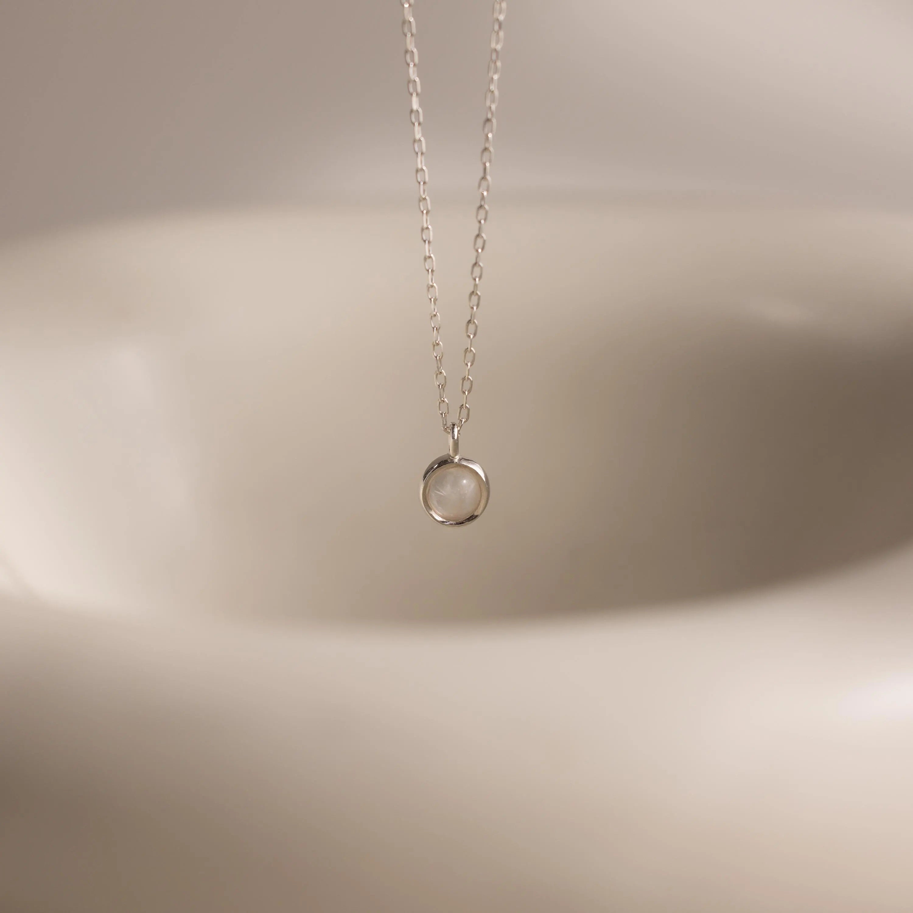 The Moonstone Charm Necklace features a delicate silver chain with a round, clear moonstone pendant—an elegant celestial accessory perfect for everyday wear.
