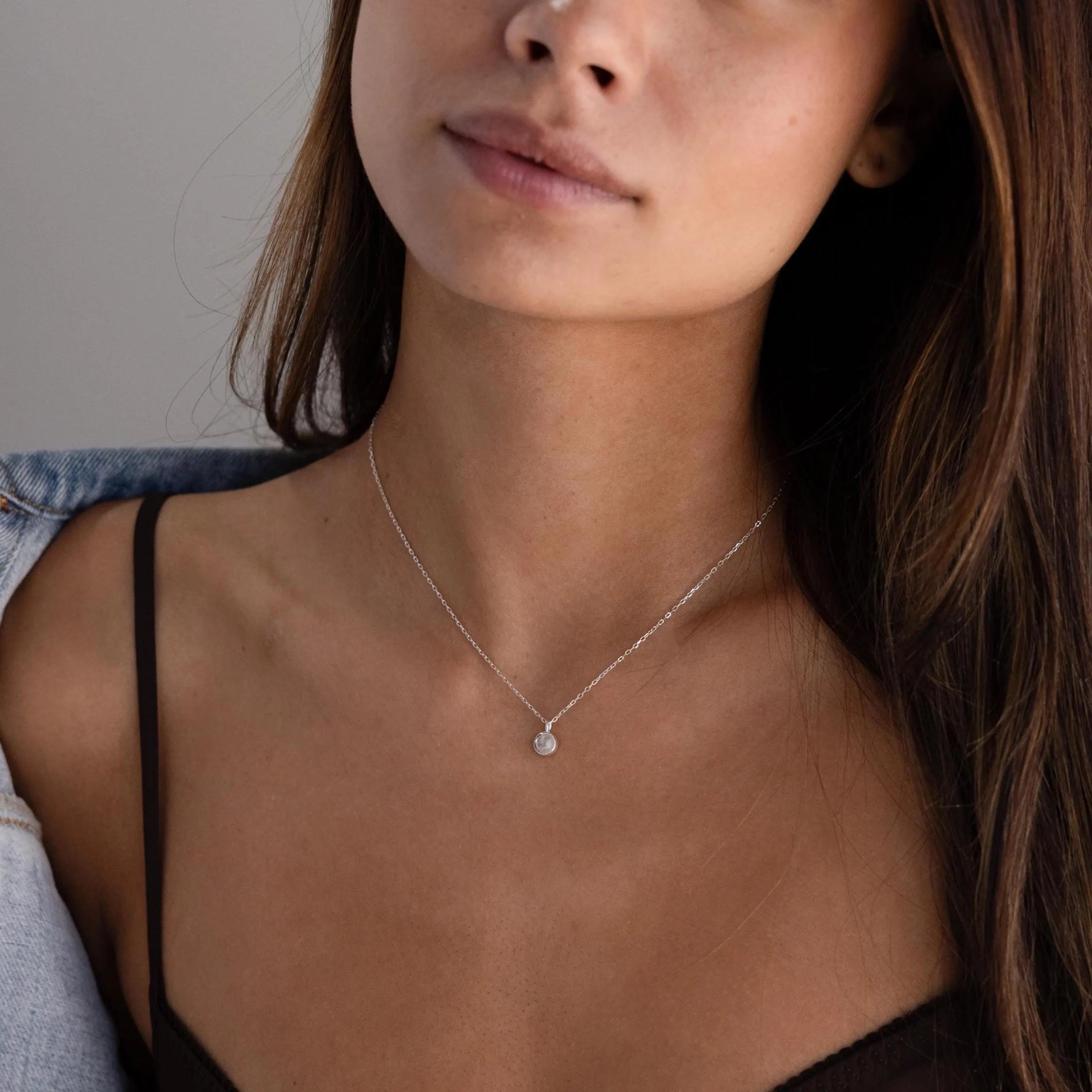 A woman wears the Moonstone Charm Necklace, featuring a small pendant, paired with a black spaghetti strap top.