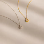 Layer these two delicate necklaces—one silver, one gold—each with a small round pendant on a light beige background. They’re perfect for stacking or pairing with your Moonstone Charm Necklace.