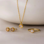 The Moonstone Charm Necklace, paired with a matching ring and stud earrings, is displayed on a light surface—ideal for anyone who loves elegant gold moonstone jewelry.