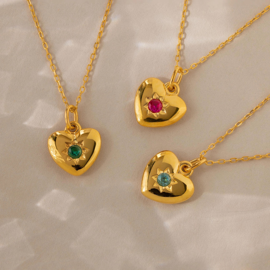Three North Star Birthstone Heart Necklaces—each with a red, green, or blue gemstone—create a charming display of personalized jewelry on a light background.