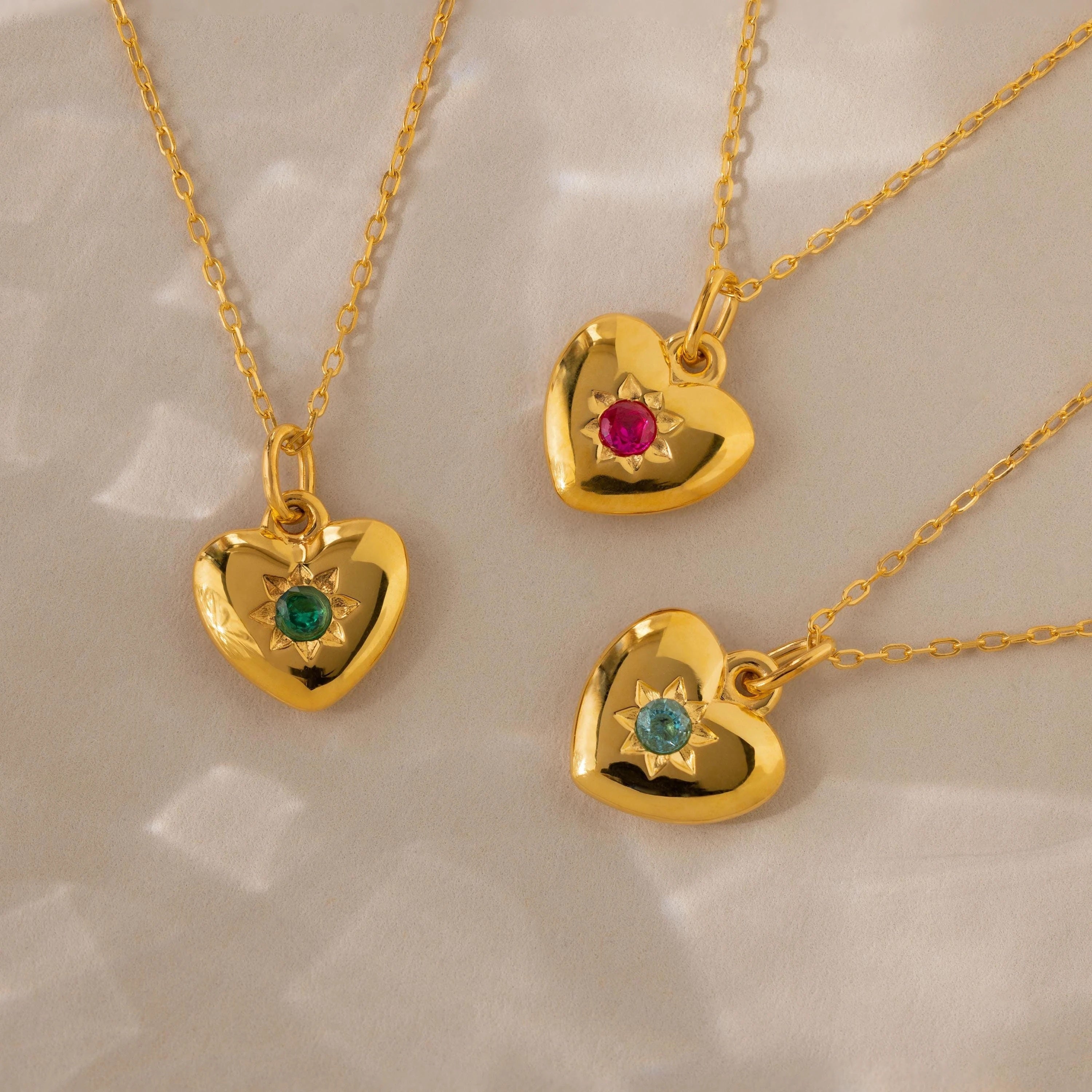 Three North Star Birthstone Heart Necklaces—each with a red, green, or blue gemstone—create a charming display of personalized jewelry on a light background.