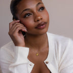 Woman in a white sweater wears the North Star Birthstone Heart Necklace, gazing up thoughtfully with her hand near her face.