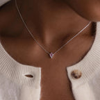 A close-up of a person wearing the Dainty Birthstone Drop Necklace with a pink pendant, styled with a white sweater.