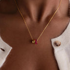 Close-up of the Duo Circle Birthstone Necklace, a gold chain featuring red and gold charms, including a circle charm, styled with a white buttoned sweater.