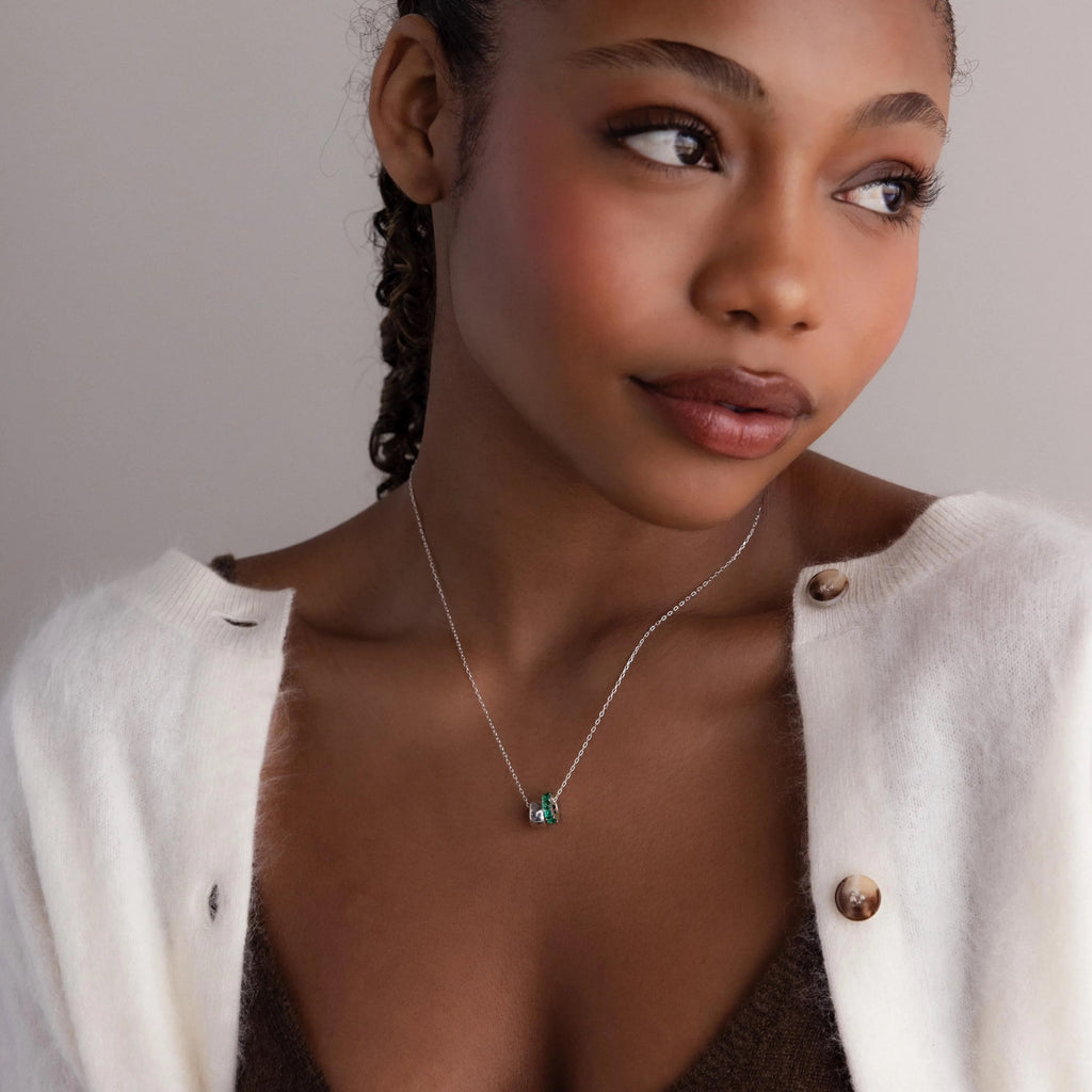 Woman in a white cardigan and brown top wears the Duo Circle Birthstone Necklace, featuring a green pendant, as she looks to the side.