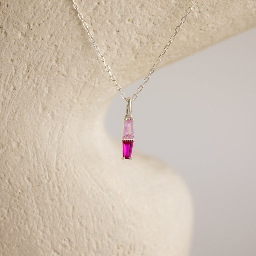 The Toi et Moi Tapered Birthstone Necklace features a delicate baguette-cut pendant with a striking pink gemstone.