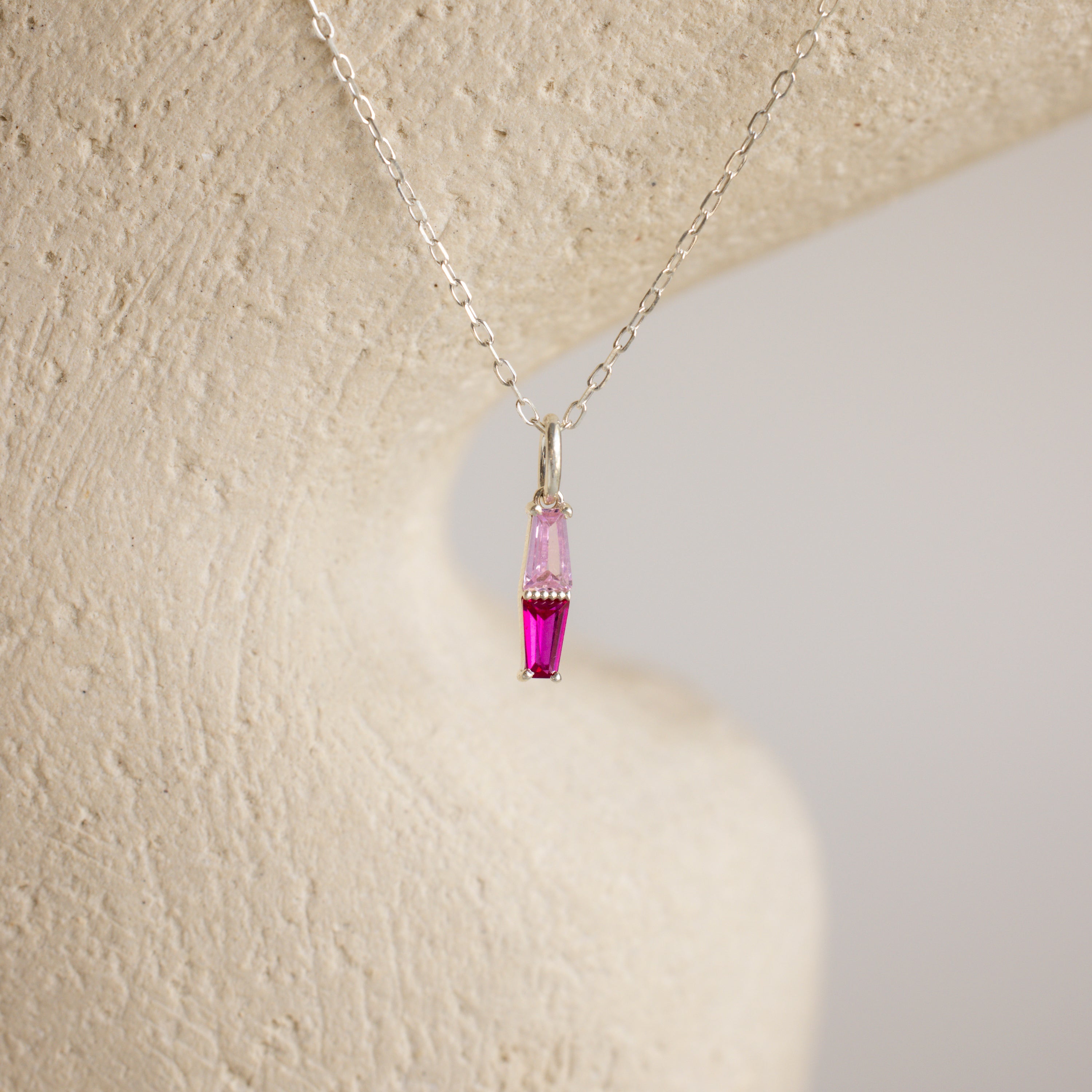 The Toi et Moi Tapered Birthstone Necklace features a delicate baguette-cut pendant with a striking pink gemstone.