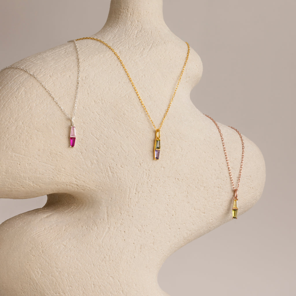 The Toi et Moi Tapered Birthstone Necklace, a dazzling colorful gemstone pendant, is elegantly draped on a textured, abstract mannequin torso.
