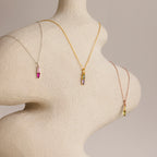The Toi et Moi Tapered Birthstone Necklace, a dazzling colorful gemstone pendant, is elegantly draped on a textured, abstract mannequin torso.