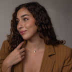 Woman with curly hair, wearing a brown pinstripe blazer and the Initial Birthstone Charm Necklace, looking to the side.