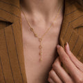 The Lariat Name Necklace, featuring gold letters for a personalized touch, adds unique style to a brown pinstripe blazer.