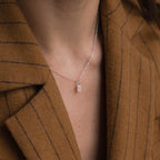 A close-up of the Pave Initial Tag Necklace featuring a rectangular pendant, styled over a brown pinstripe blazer for a personalized accent.