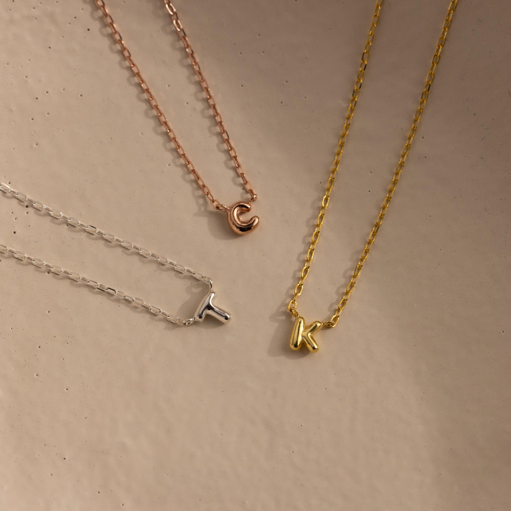 Rose gold letter C, silver letter T and gold letter K bubble initial necklaces.