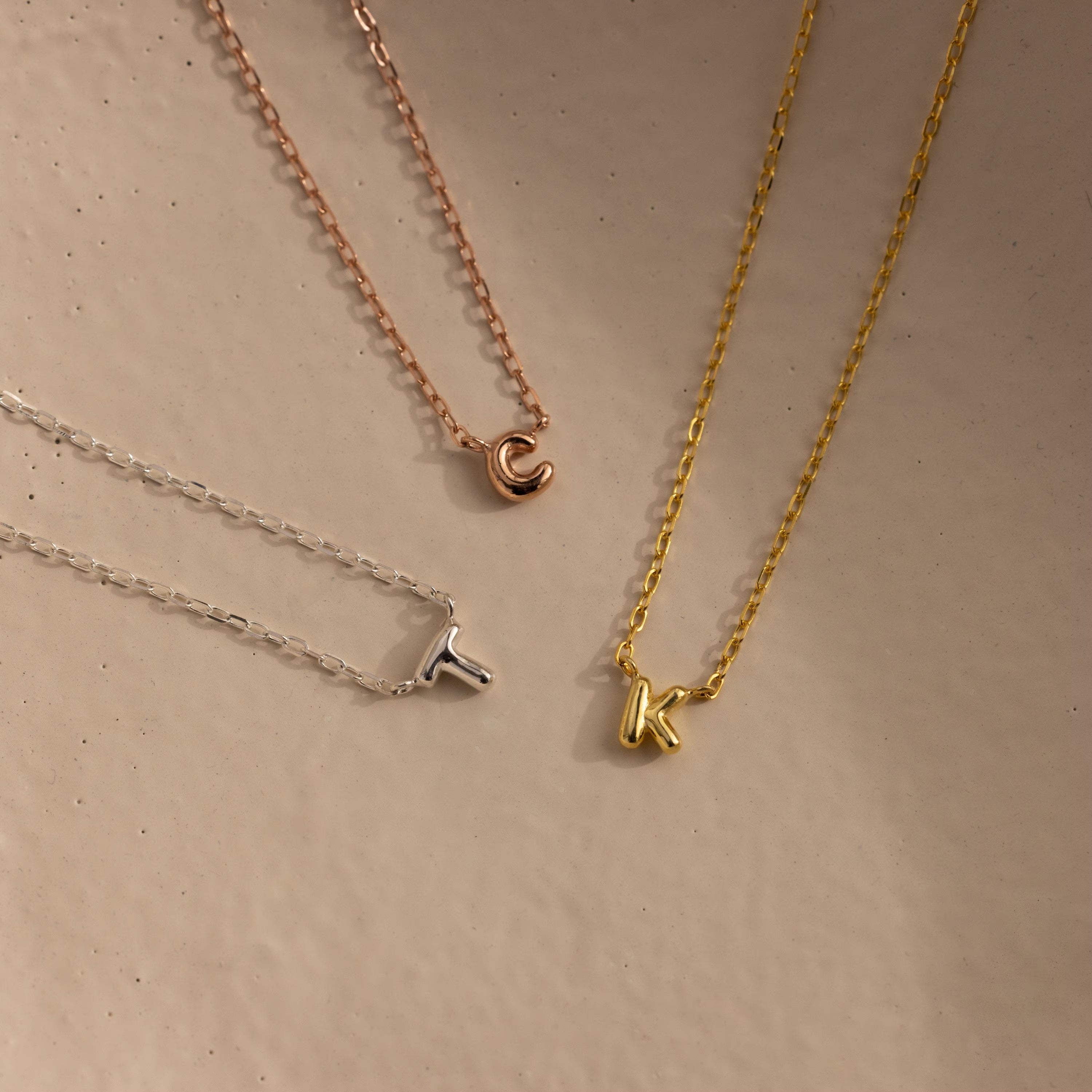 Rose gold letter C, silver letter T and gold letter K bubble initial necklaces.