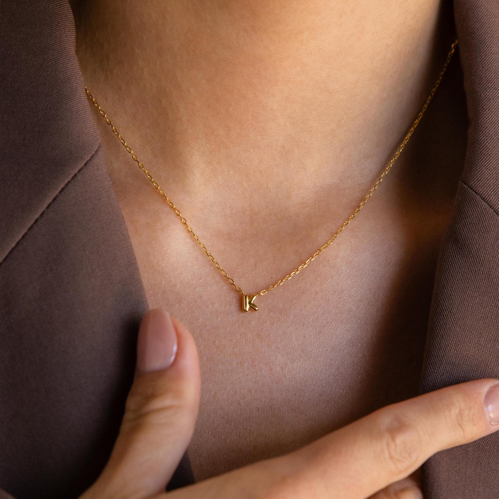Model wearing a gold Custom Bubble Initial Necklace with the letter K, styled with a brown blazer.