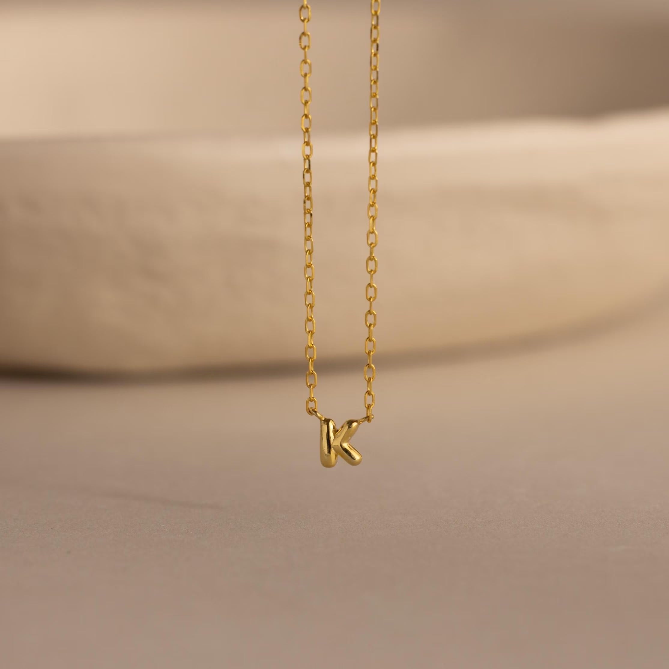 Close-up of the gold Custom Bubble Initial Necklace with the letter K, displayed on a neutral surface.