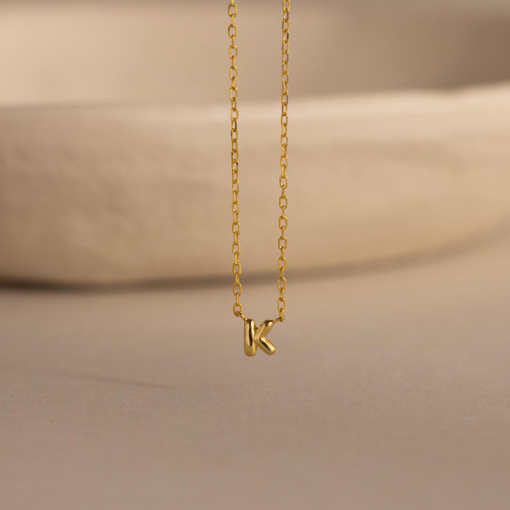 Close-up of the gold Custom Bubble Initial Necklace with the letter K, displayed on a neutral surface.