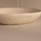 Silver dainty bubble initial M charm necklace against a neutral background.