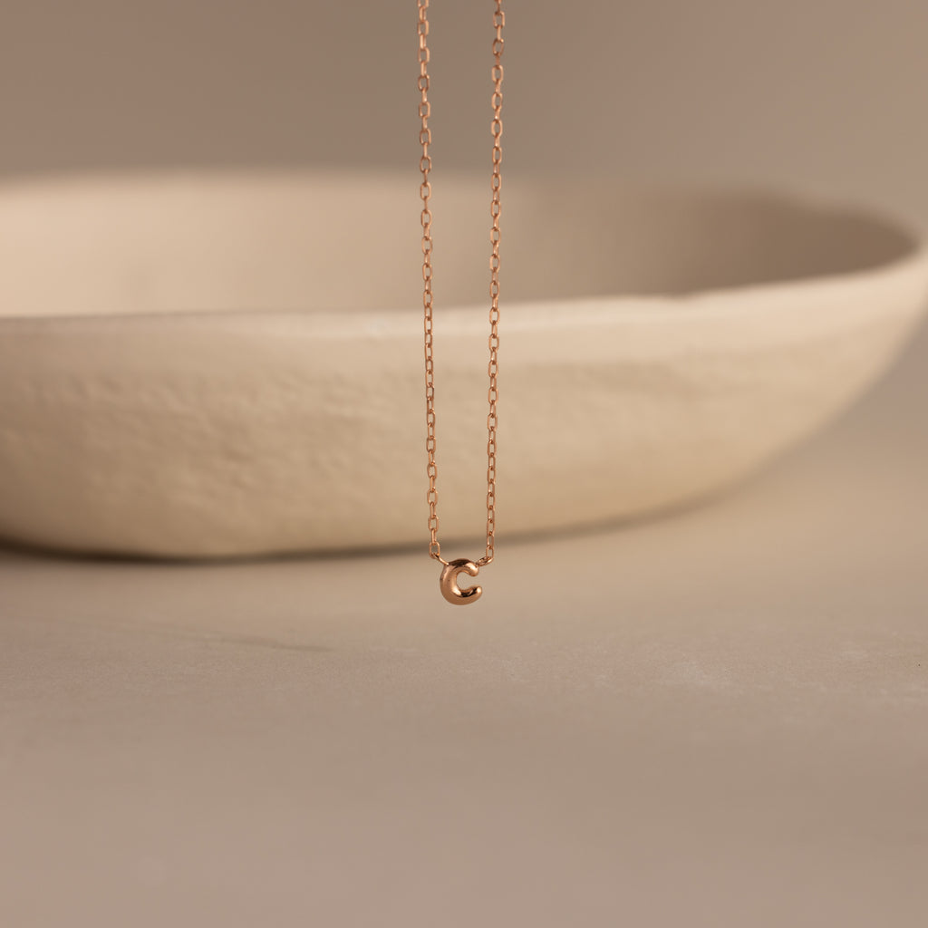 Rose gold dainty bubble initial C charm necklace against a neutral background.