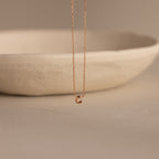 Rose gold dainty bubble initial C charm necklace against a neutral background.