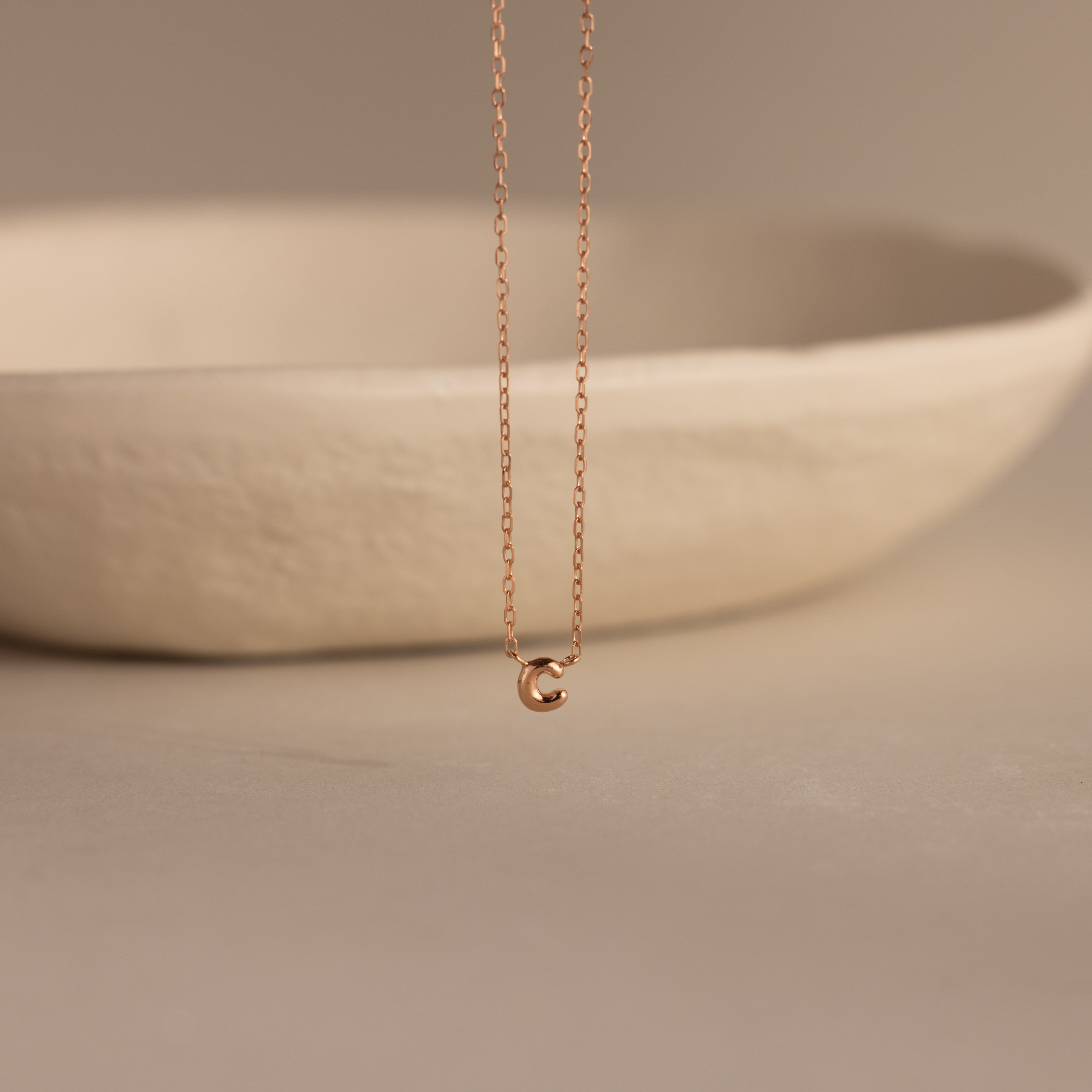 Rose gold dainty bubble initial C charm necklace against a neutral background.