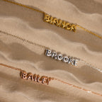 Gold Bianca bubble name necklace, silver Brooke necklace and rose gold Bailey necklace laying on sand.