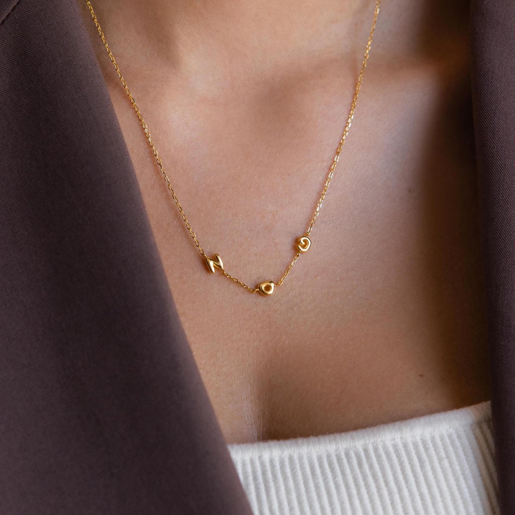 Close up of model wearing a Bubble Letter Necklace featuring three individual gold bubble letters, N O G, on a fine cable chain. The letters are soft, rounded and dainty with a smooth finish.