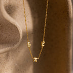 Gold bubble letter necklace spelling “BEK” styled against a sculpted ceramic surface.