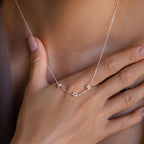 Silver bubble letter necklace spelling “MDH” worn close to the neckline with a hand resting on the chest.