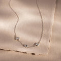 Silver bubble letter necklace spelling MDH lying on a fabric surface.