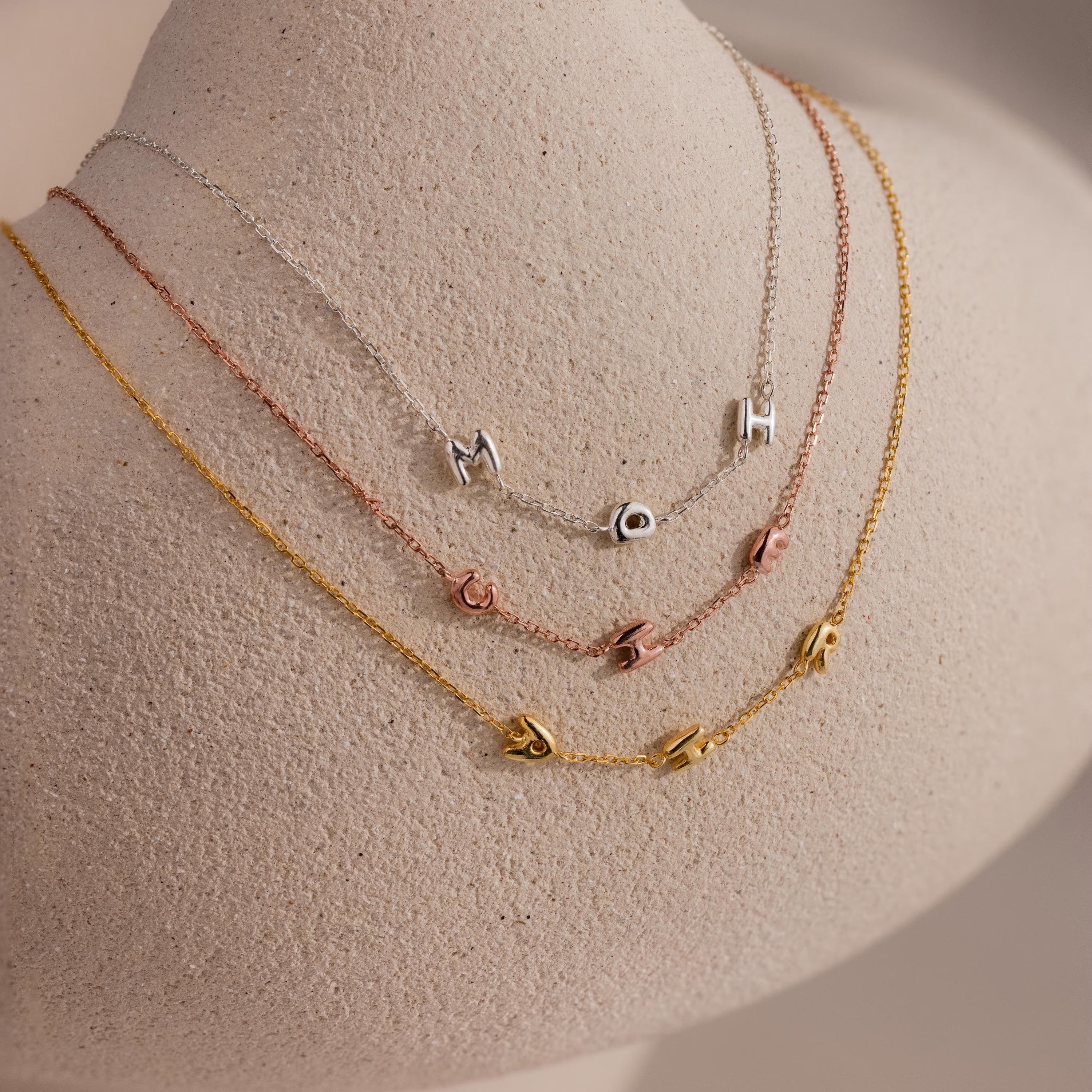 The Multiple Bubble Letter Necklace, shown with custom charms spelling MOH, curz, and jana on a neutral mannequin, offers a playful boho vibe—perfect for personalizing your style.