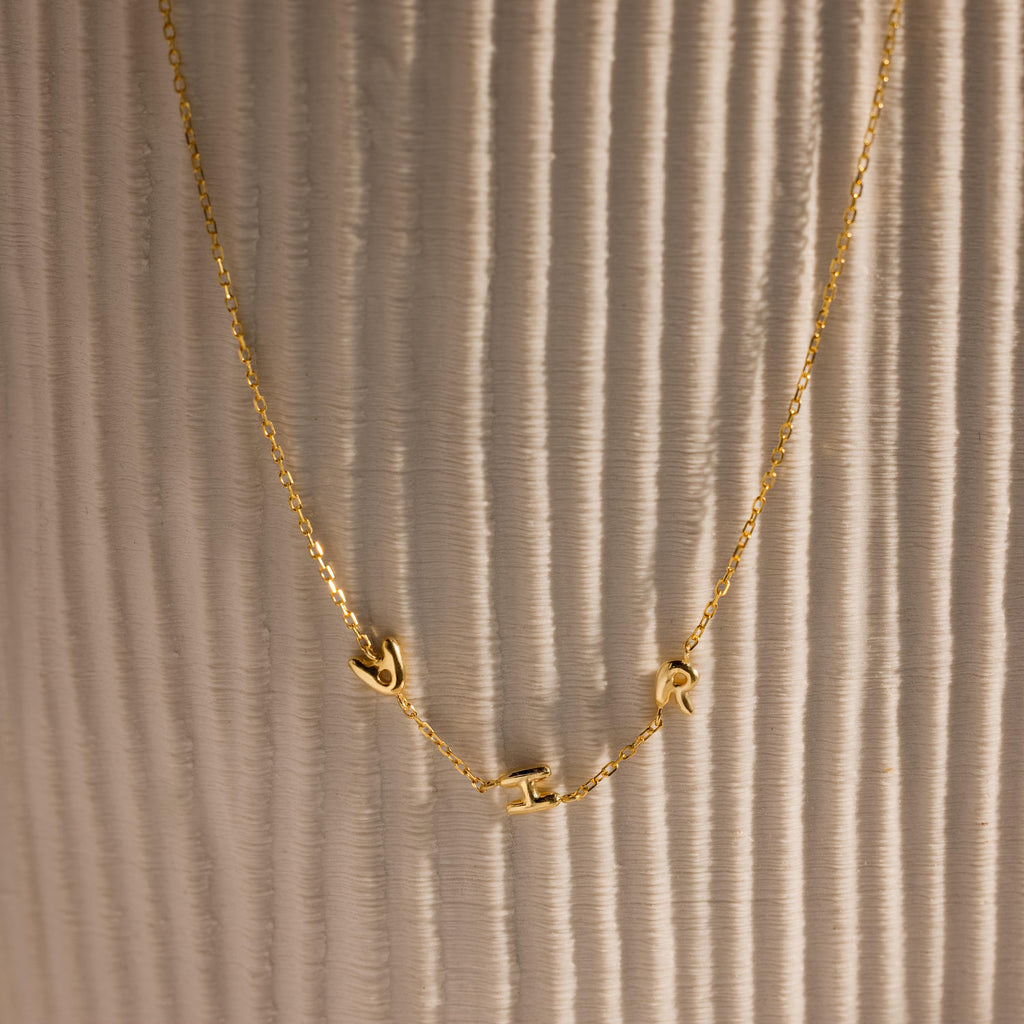 Gold bubble letter necklace spelling AHR on vase.