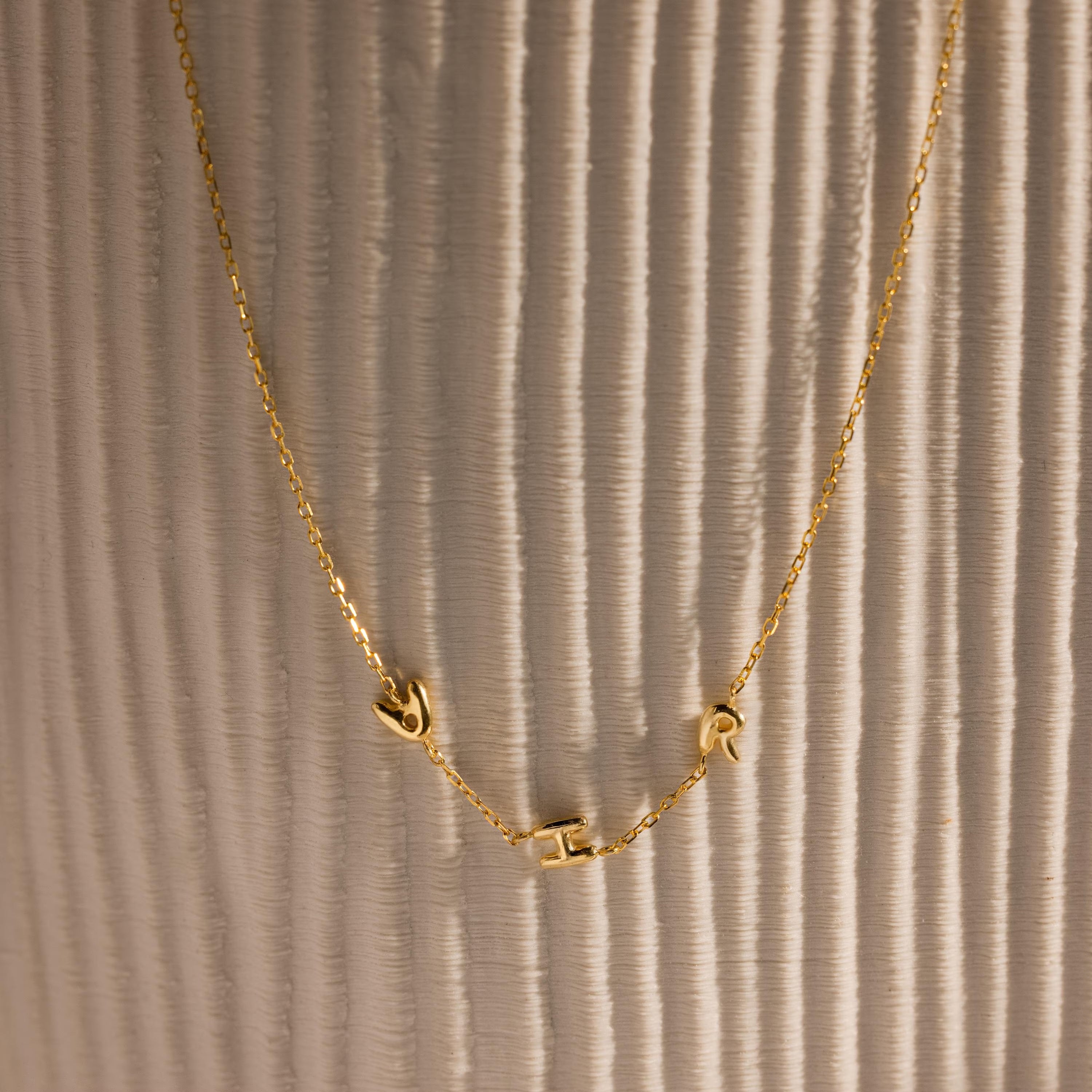 Gold bubble letter necklace spelling AHR on vase.