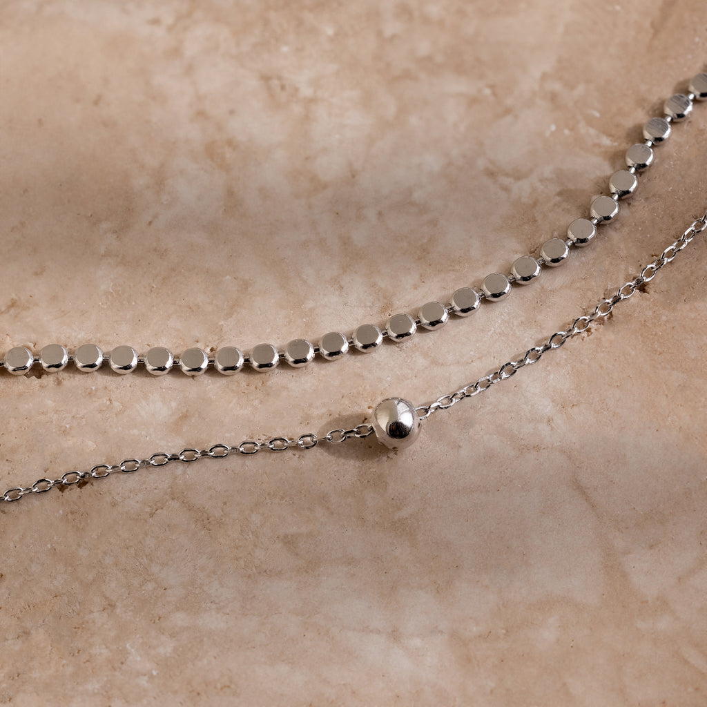 Silver beaded chain necklace on a beige stone surface