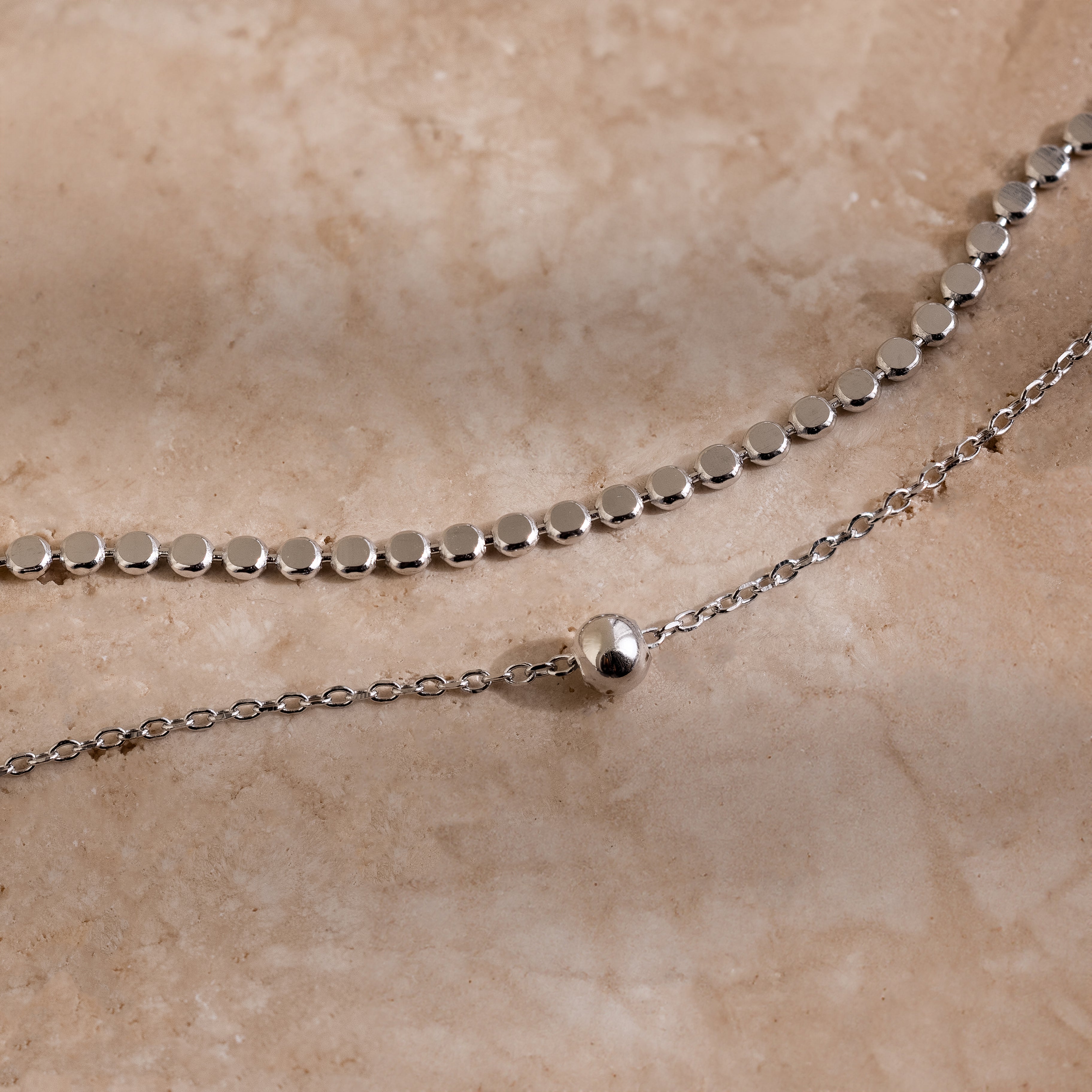 Silver beaded chain necklace on a beige stone surface