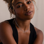 Woman wearing a black sleeveless top and silver beaded double chain layered necklace against a neutral background