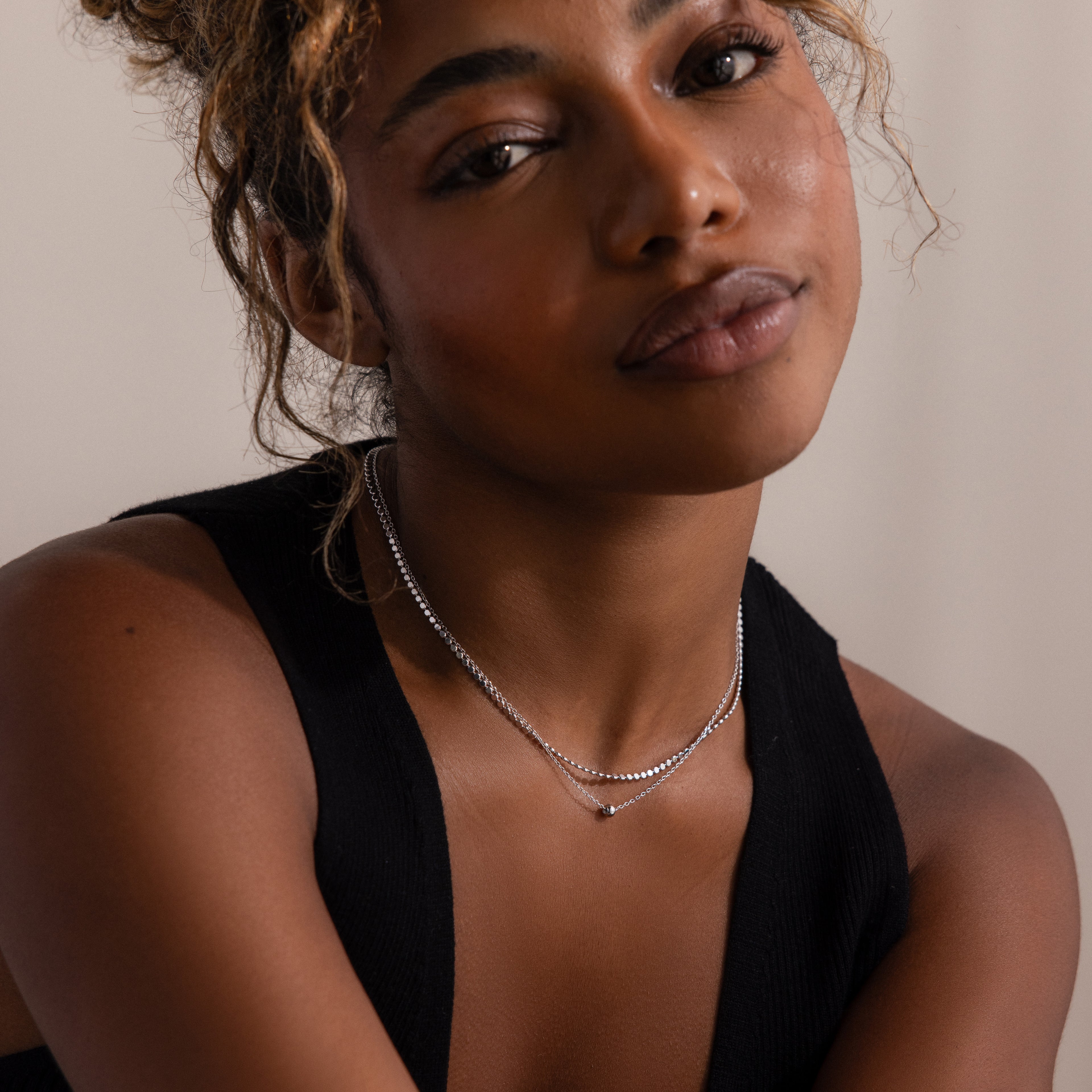 Woman wearing a black sleeveless top and silver beaded double chain layered necklace against a neutral background