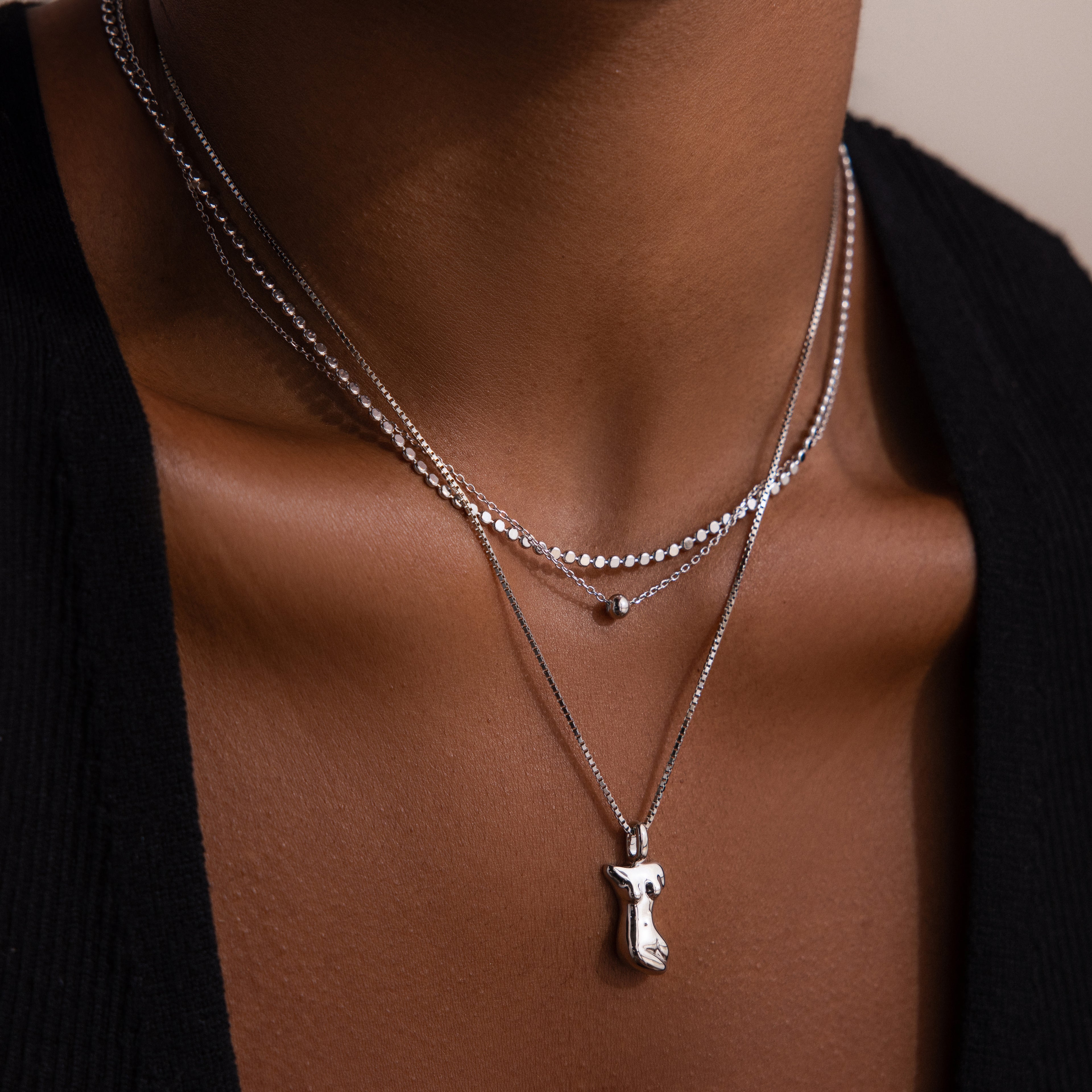 Layered silver necklaces with a pendant on a woman wearing a black top.