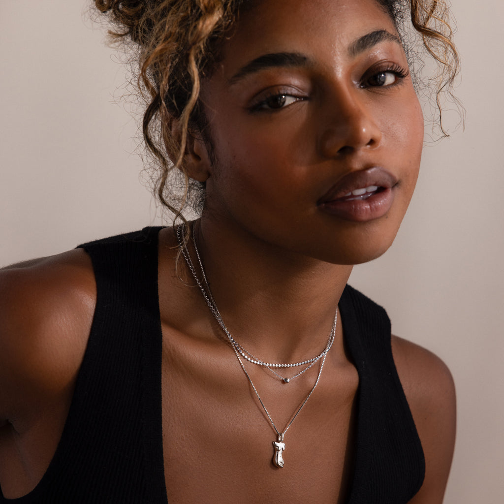 Woman wearing a black top and layered silver necklaces against a neutral background