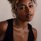 Woman wearing a black top and layered silver necklaces against a neutral background