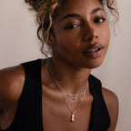 Woman wearing a black top and layered silver necklaces against a neutral background