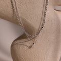 Silver beaded double chain necklace on a beige stone background