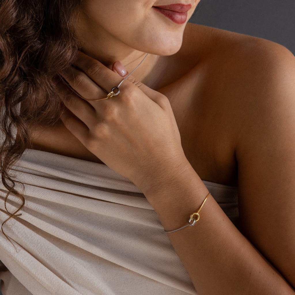 Woman models the Interlocking Circles Necklace and Bracelet Set—featuring gold and silver mixed metals—with a matching interlocking circles ring, styled with a soft beige off-shoulder top.
