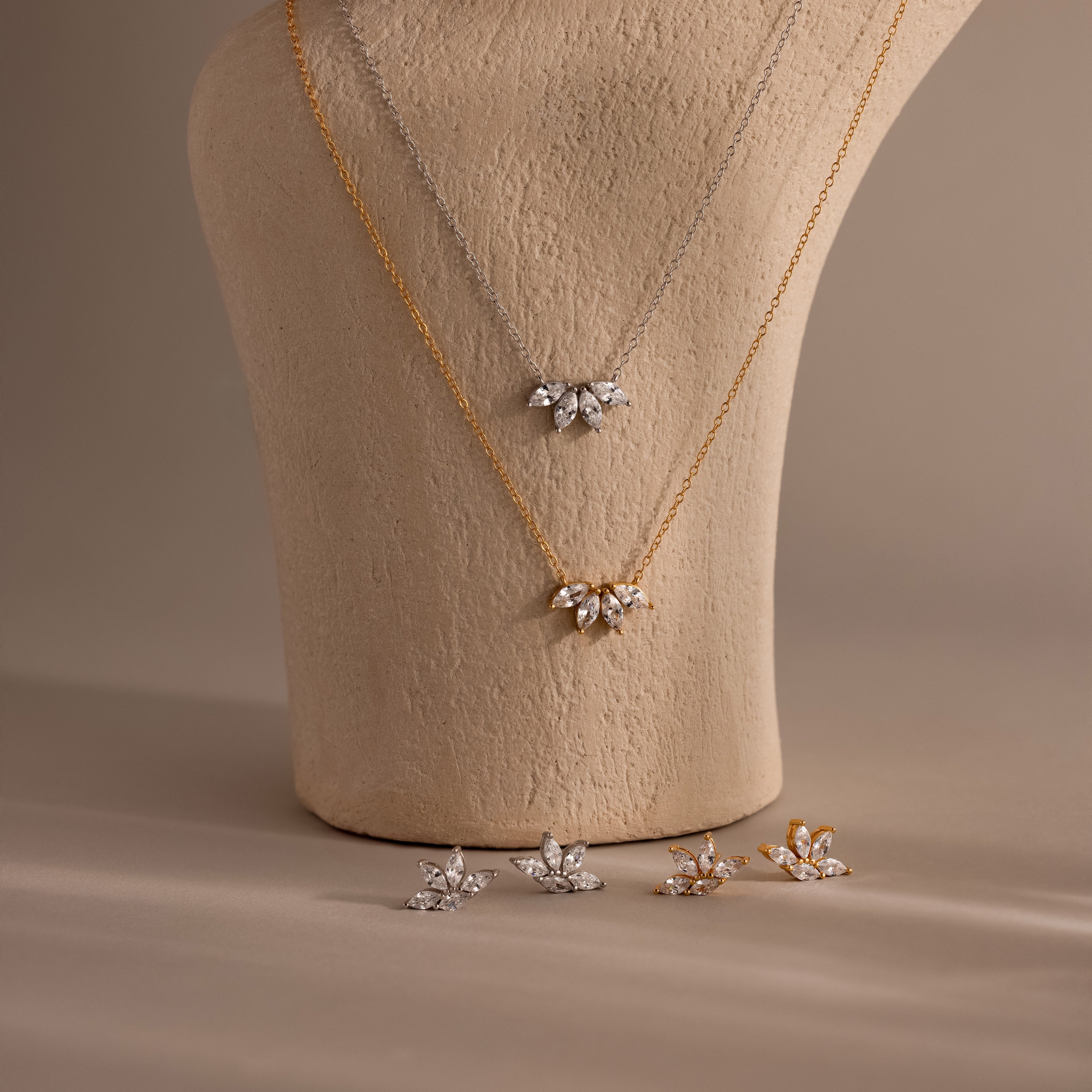 The Marquise Diamond Jewelry Set, featuring gold and silver leaf-shaped necklaces and matching earrings, is elegantly displayed on a beige bust—an ideal choice for sophisticated wedding jewelry.
