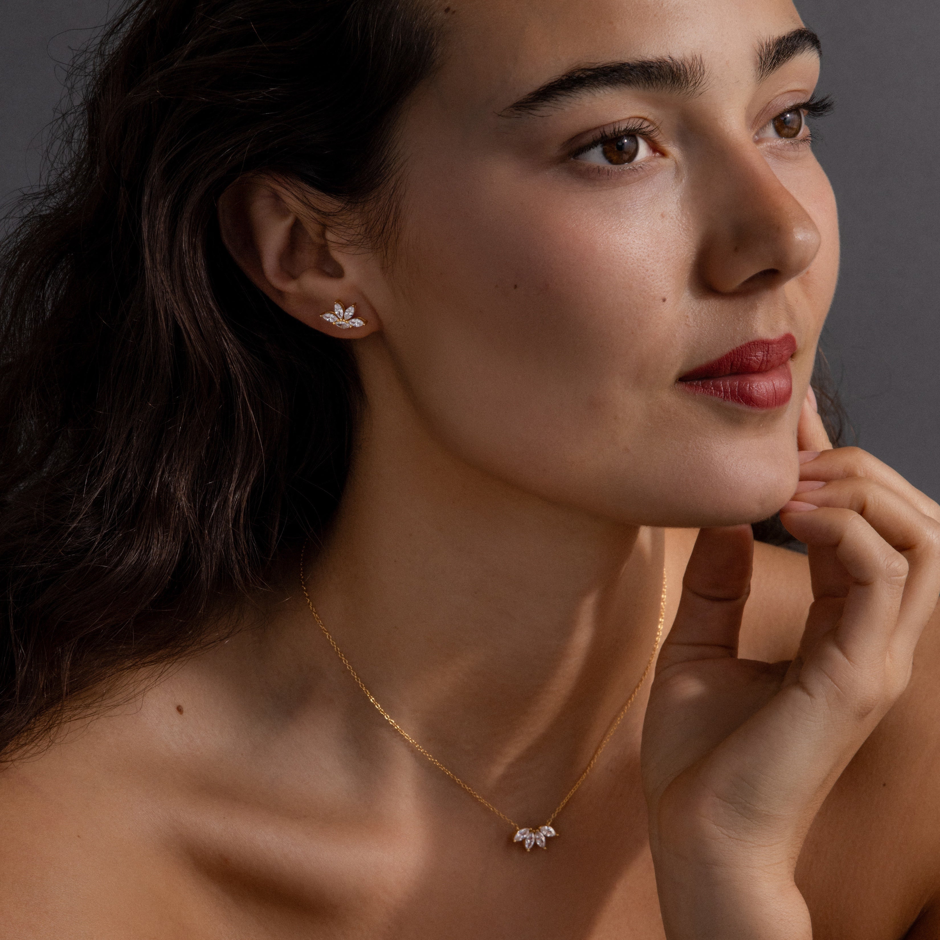 A woman wears the Marquise Diamond Jewelry Set in 18K Gold—featuring a gold necklace and floral earrings—as she smiles slightly, making it an elegant wedding gift choice.