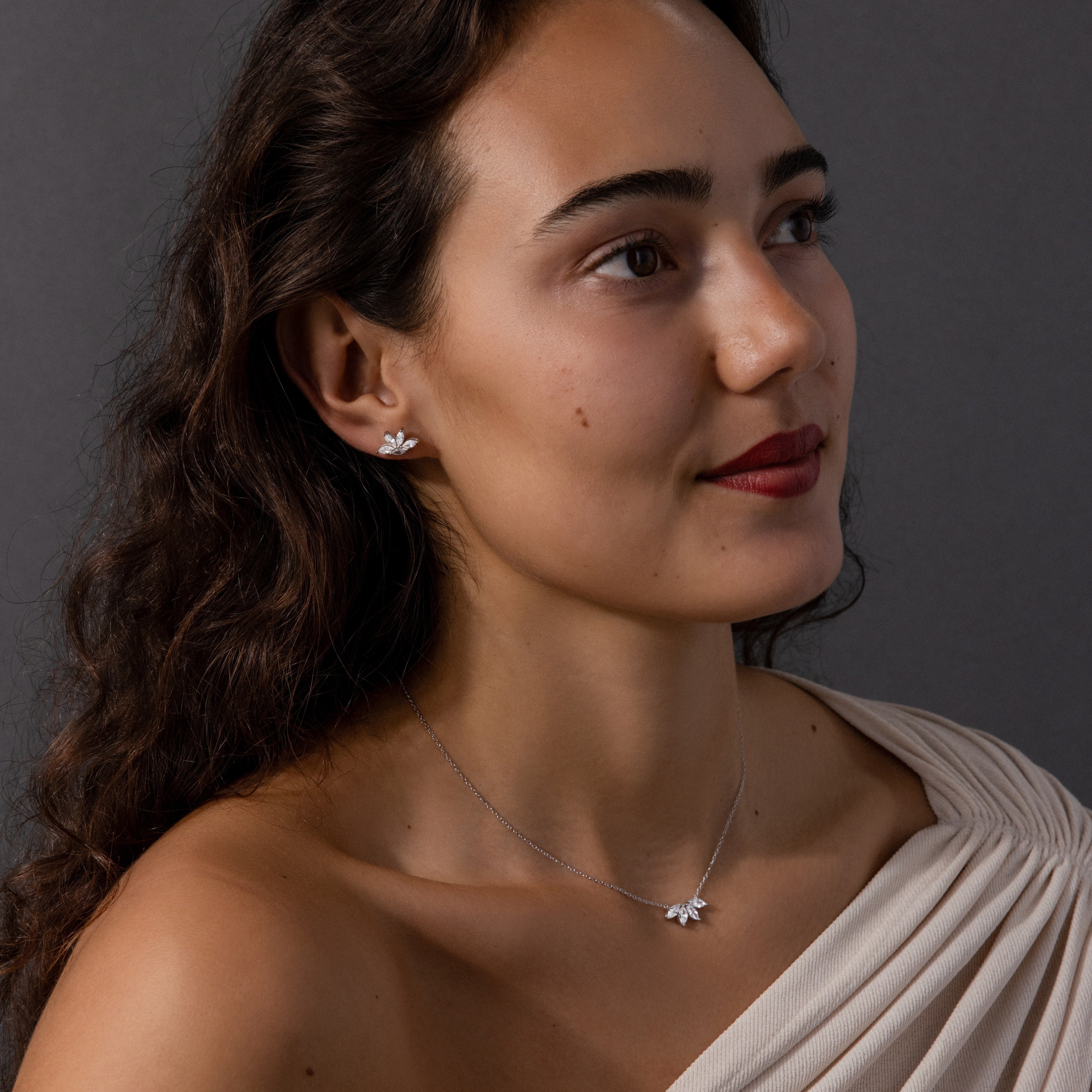 Woman with long dark hair wearing a cream off-shoulder top, silver lotus earrings, and the Marquise Diamond Jewelry Set in Sterling Silver—a matching necklace set ideal for elegant bridal jewelry.