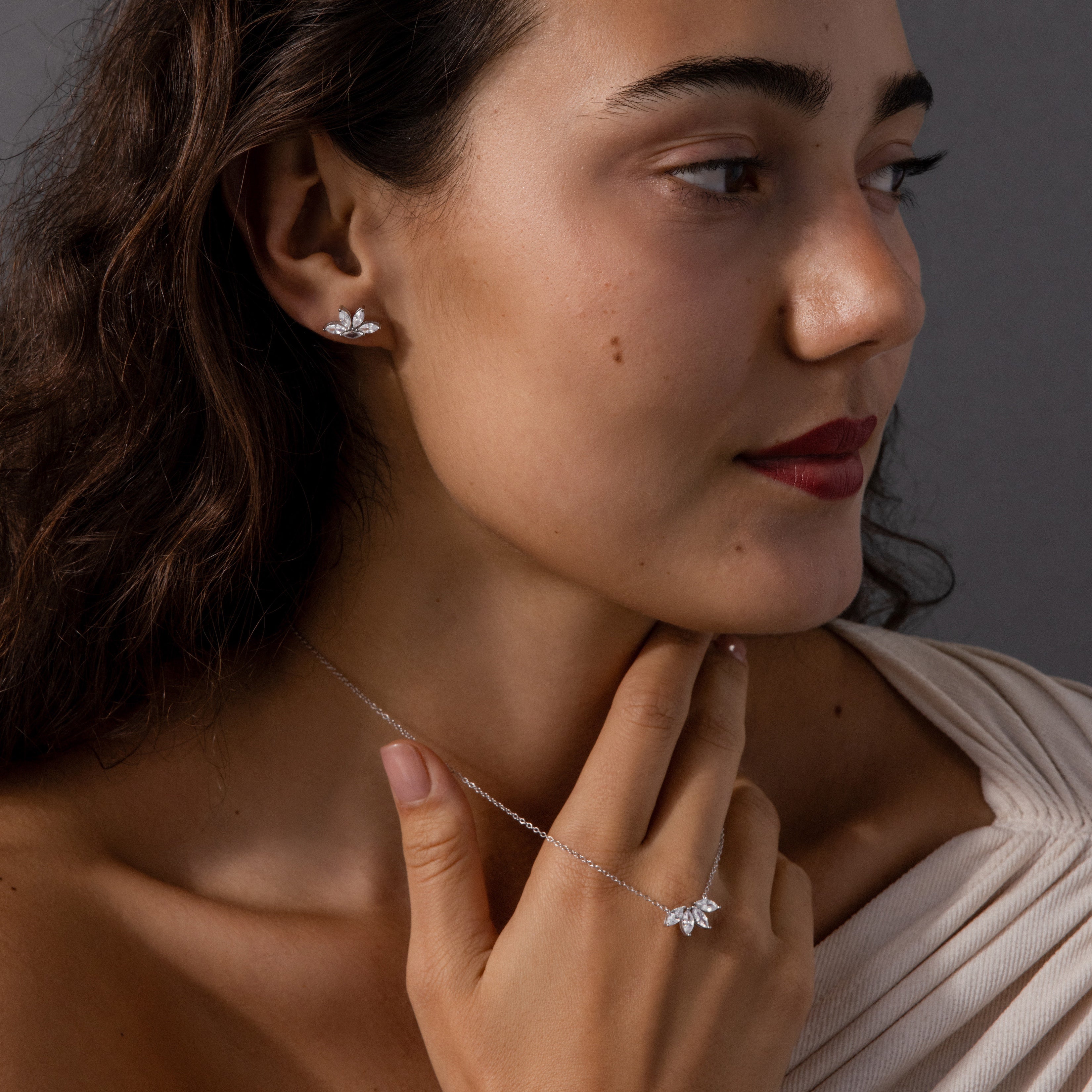 A woman wearing the Marquise Diamond Jewelry Set in Sterling Silver—featuring leaf earrings and a diamond necklace—gently touches her neck while looking to the side, making an elegant bridal jewelry statement.